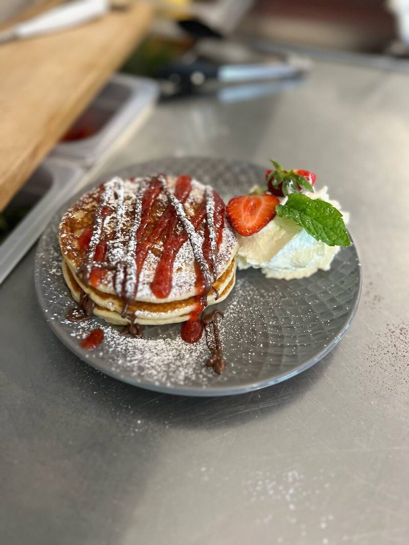 Tre amerikanska pannkakor med grädde, sylt, chokladsås och färska bär